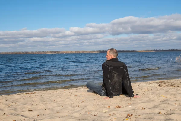 Hiker man sitting on the beach, back to camera, smiling, relaxin