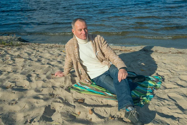 Pohledný muž, oblečený nedbale, sedí na pobřeží a dívá se — Stock fotografie