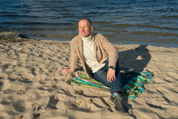 Neşeli gülümseyen adam, rahat giyen, sahilde oturan, looki