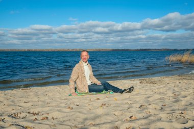 Neşeli adam, rahat giyen, sahilde oturan, rahatlatıcı ve