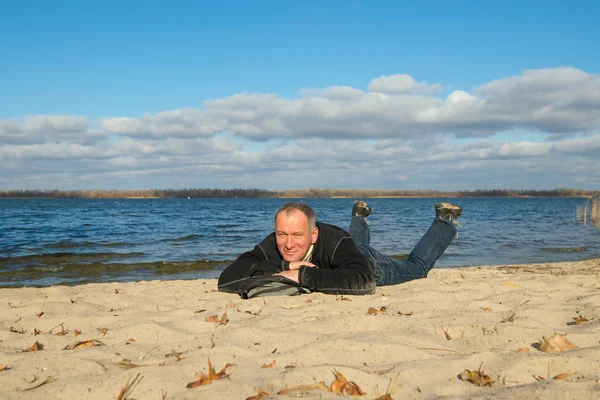 Turysta człowieka na wybrzeżu, leżące na piasku, uśmiechając się wygląd — Zdjęcie stockowe