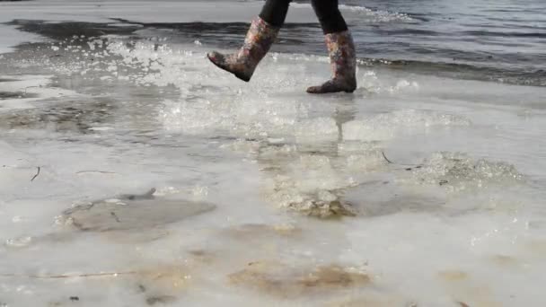 Mulher de botas de borracha brilhante caminha na borda do surf e gelo — Vídeo de Stock