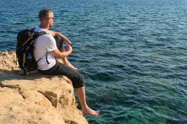 Dinlenme uzun yürüyüşe çıkan kimse bir kayalık deniz kıyısında oturur