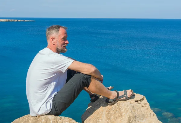 Mosolygó ember ül a sziklás tengerparton — Stock Fotó
