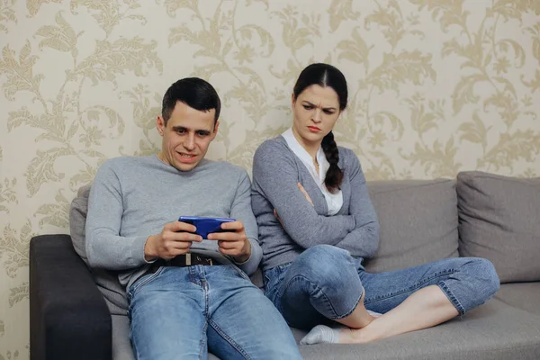 Gamer husband plays on smartphone, angry wife sits nearby