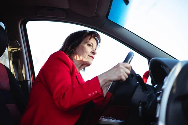 An elderly business woman is driving her car. Peeks out on the main road