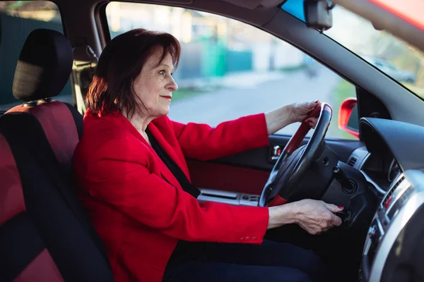 An elderly business woman is driving her car. Peeks out on the main road