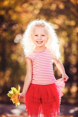 Sarı yaprakların arkasında gülümseyen küçük bir kız.