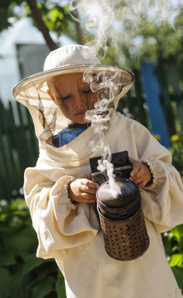 Young beekeeper boy using a smoker on bee yard