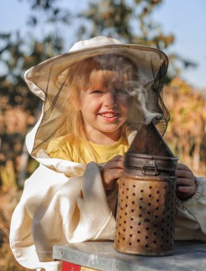 Little girl beekeeper blows smoker for bees clipart