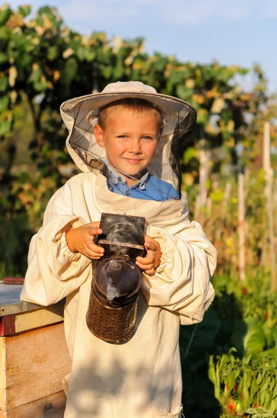 Imker-Porträt eines kleinen Jungen, der im Bienenstock mit Raucher für Bienen in der Hand arbeitet — Stockfoto