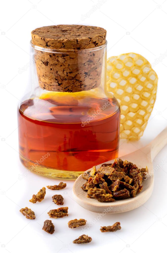 A bottle of propolis tincture and a wooden spoon of propolis granules. Medical preparations bee propolis. Apitherapy. Isolated on white background. Bee glue. Apitherapy
