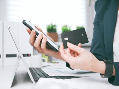 Kredi kartı tutan, dizüstü bilgisayar ve akıllı telefon kullanan genç bir kadın. Çevrimiçi alışveriş, rezervasyon ve bankacılık konsepti. İş kadını ya da girişimci iç işlerinde çalışıyor.