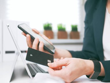 Kredi kartı tutan, dizüstü bilgisayar ve akıllı telefon kullanan genç bir kadın. Çevrimiçi alışveriş, rezervasyon ve bankacılık konsepti. İş kadını ya da girişimci iç işlerinde çalışıyor..