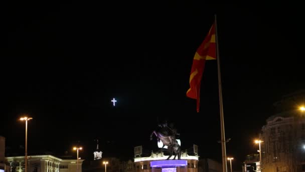 SKOPJE MACEDONIA - JULY 2015: Alexander the Great arca, bendera Makedonia dan salib besar dalam bingkai yang sama pada malam hari di pusat kota Skopje . — Stok Video