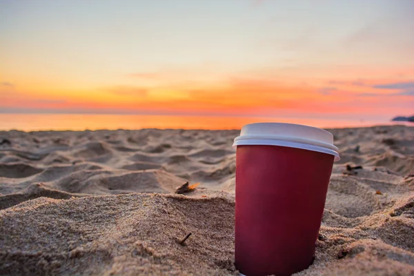 Close up of coffee cup on sandy beach at sunrise or sunset — Stock Photo, Image