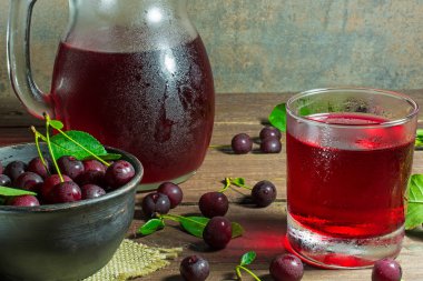 cold cherry juice in a glass and pitcher on wooden table clipart