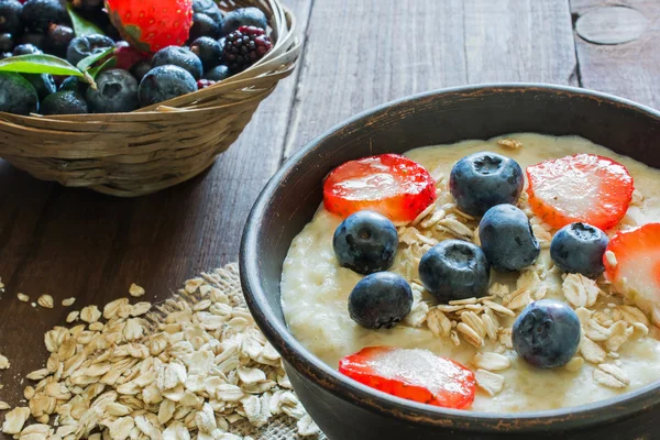 Oatmeal porridge in brown ceramic bowl with ripe berries — Stock Photo, Image