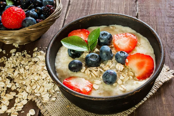 Oatmeal porridge in brown pottery bowl with ripe berries. healthy breakfast — Stock Photo, Image