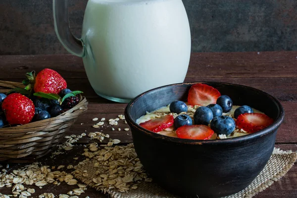 Leche en una jarra y gachas de avena con bayas frescas maduras — Foto de Stock