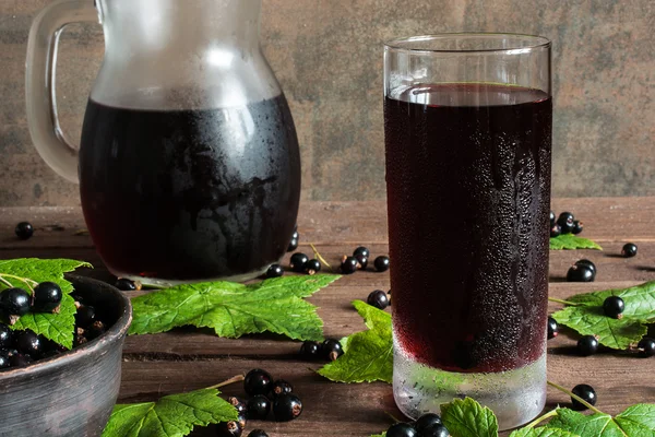 Cold black currant juice in a glass and pitcher on wooden table — Stock Photo, Image
