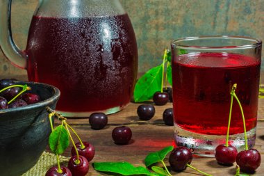 cold cherry juice in a glass and pitcher on wooden table with ripe berries in pottery bowl clipart