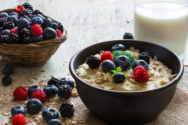 Farinata d'avena porridge in ciotola rustica con bacche fresche mature e bicchiere di latte. colazione sana — Foto Stock