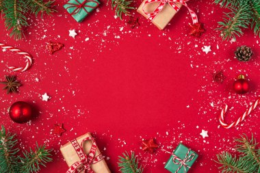 Kırmızı arka planda Noel kompozisyonu. Hediyelerden yapılmış çerçeve, köknar ağacı, şeker, süslemeler. Noel, kış, yeni yıl konsepti. Düz konum, kopyalama alanı olan üst görünüm
