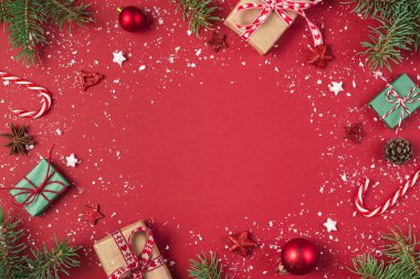 Noel ya da Mutlu Yıllar kompozisyonu. Köknar dallarından yapılmış çerçeve, hediye kutuları ve kırmızı arka planda tatil süslemeleri. Düz yat. Kopyalama alanı olan üst görünüm