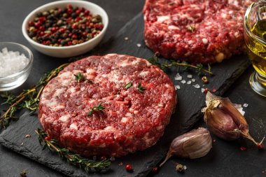 Siyah arka planda pişirmek için baharat ve otlarla birlikte siyah tahtada taze kıymalı biftek köfteleri. Kapat.