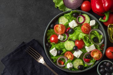 Yunan salatası. Taze sebzelerden sebze salatası, beyaz peynir ve siyah masada çatalla birlikte havlunun üzerinde zeytin. Üst Manzara. Vejetaryen gıda konsepti