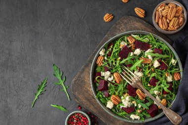 Arugula, pancar ve fındıklı mavi peynir salatası ve siyah masa arka planında çatal var. Kopyalama alanı olan üst görünüm. sağlıklı vejetaryen yemekleri