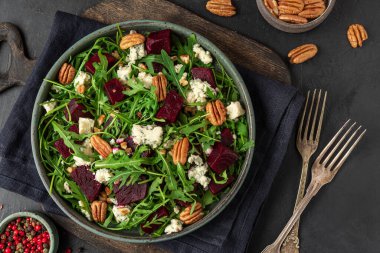Taze roka, pancar kökü, gorgonzola peyniri ve siyah arka planda çatallı fındıklı salata. Üst Manzara. Sağlıklı vejetaryen yemeği. Kapat.