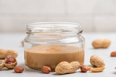 Fıstık ezmesi kavanozu ve beyaz arka planda bir yığın fındık. Organik vejetaryen yemeği. Lezzetli bir kahvaltı. Kapat.