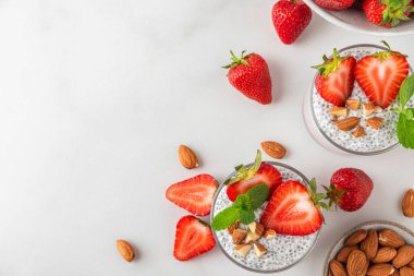 Vejetaryen kahvaltısı. Bardakta Chia pudingi, taze çilek, fındık ve naneli beyaz arka plan. Kopyalama alanı olan üst görünüm. Sağlıklı yemek.