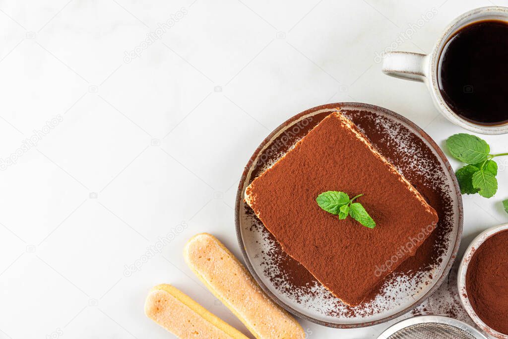 Italian homemade tiramisu cake with fresh mint on plate and coffee cup over white background. Top view with copy space. Delicious no bake dessert for tasty breakfast