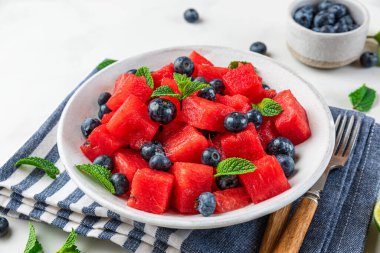 Beyaz arka planda peçetenin üzerinde nane ve limon suyu ile karpuz ve yaban mersini salatası. Kapat. Yaz yemeklerini tazeliyorum.