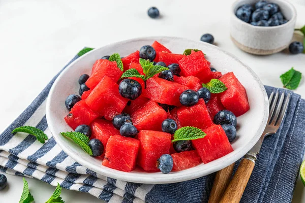 Beyaz arka planda peçetenin üzerinde nane ve limon suyu ile karpuz ve yaban mersini salatası. Kapat. Yaz yemeklerini tazeliyorum.