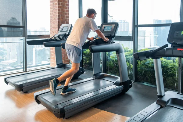 Modern spor salonunda şehir manzaralı koşu bandında çalışan bir adam. Erkek kardiyo yapıyor, spor eğitmeni üzerinde egzersiz yapıyor ve konut binasındaki spor salonunda koşu bandında koşuyor. Sağlık, sağlık, sağlık.