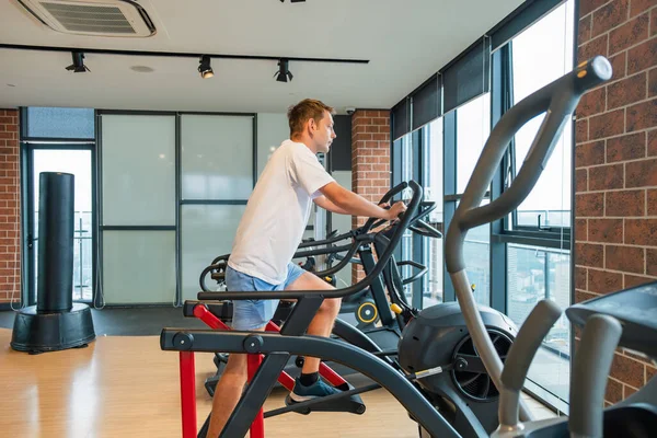 Modern spor salonunda şehir manzaralı eliptik bir antrenörde çalışan bir adam. Erkek, konut binasındaki fitness stüdyosunda sabit egzersiz bisikleti üzerinde kardiyo eğitimi alıyor. Zindelik, sağlık