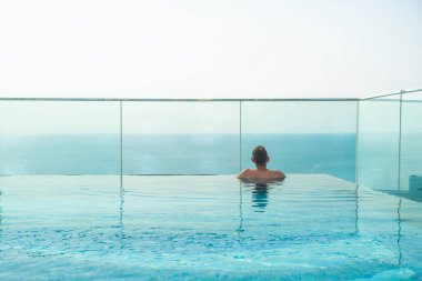 İnsanoğlu sonsuz çatı havuzunda sonsuz okyanus ufkunun altında Phu Quoc tropikal adasında, Vietnam 'da dinleniyor. Erkek havadan deniz manzarasının tadını çıkarır. Tatil, dinlenme, tropik tatil ve seyahat