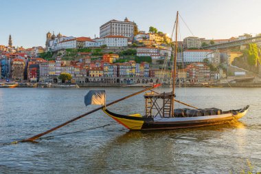 Douro Nehri 'ndeki geleneksel haham teknesi renkli Ribeira bölgesiyle ve Portekiz' in Porto şehrindeki tarihi binalarıyla. Gün doğumunda Clerigos Kulesi ve Dom Luis Köprüsü ile tepe kenti manzarası. seyahat
