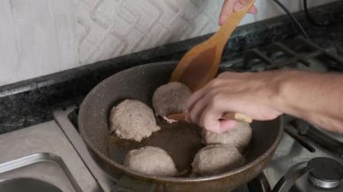 Adam yemek pişirirken köfteyi tavada çeviriyor. Ev mutfağında aşçılık, yemek hazırlama ve aşçılık süreci.