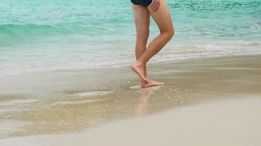 Tayland 'ın Phuket adasındaki kayalık kıyıların yakınındaki sığ tropikal deniz suyunda kumlu sahilde yürüyen mayo giymiş bir adam. Özgürlük plajında yalnız erkek turist. Popüler yaz ve kış tatilleri