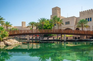 Dubai, BAE 'deki Madinat Jumeirah' da taş binalar, palmiye ağaçları ve ahşap bir köprüyle geleneksel Arap tarzı mimari. Birleşik Arap Emirlikleri 'nde seyahat ve turistik dönüm noktası.