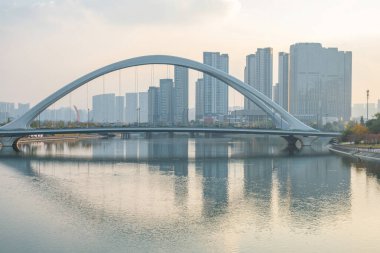 Chengdu, Sichuan eyaletinde günbatımında modern şehir silueti olan sakin bir nehri kapsayan modern kemer köprüsü. Modern şehir altyapısı ve Asya 'daki akıllı şehir gelişimi.