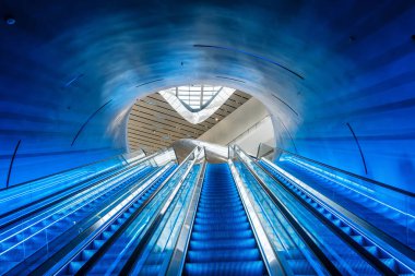 Çin 'in Chengdu şehrinde mimari perspektifi simetriye sahip eğimli modern tünelde, gelecekçi mavi aydınlatma yürüyen merdivenleri. Simetri, minimalizm teknolojisi, yenilik ve modernlik. Soyut