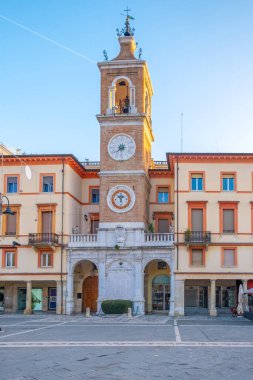 Rimini 'deki Piazza Tre Martiri' deki tarihi saat kulesi güneş doğarken İtalya 'nın Emilia Romagna şehrinde pastel cepheleri ve atari salonlarıyla. İtalyan mimarisi. Dikey oryantasyon. Seyahat hedefi.