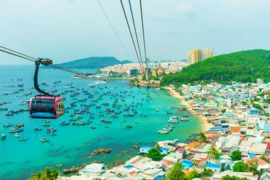 Vietnam 'daki Phu Quoc adasındaki An Thoi limanı yakınlarında turkuaz su ve balıkçı tekneleri üzerinde seyahat eden kablo araç kabini. Ada ulaşımı ve turizm altyapısı Modern Hon Thom teleferik gondolları.