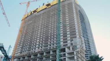 Gökyüzüne karşı vinçleri ve iskelesi olan yüksek binalar inşa ediliyor. Kentsel gelişim ve modern mimari. İnşaat endüstrisi, mühendislik ve ilerleme. Düşük açı görünümü.